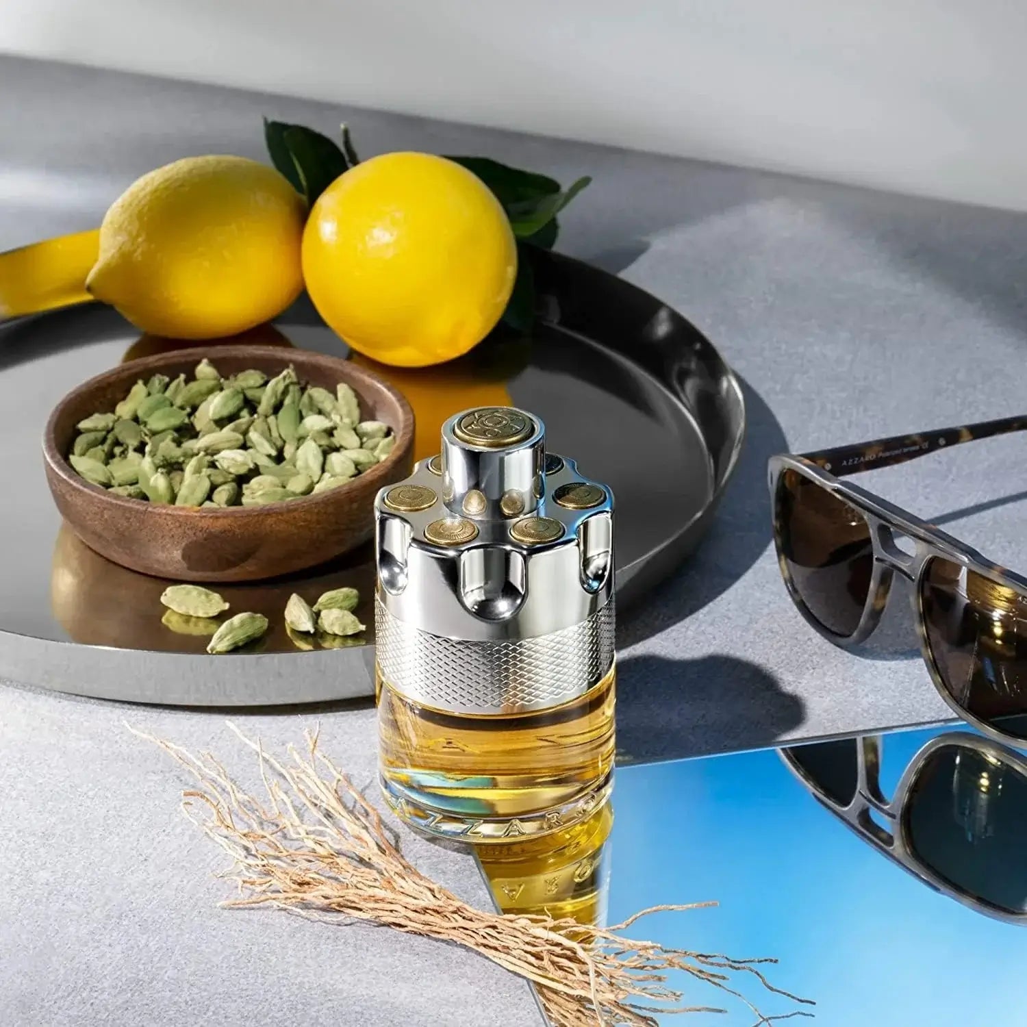 Perfume bottle with lemons, green leaves, and sunglasses on a reflective surface